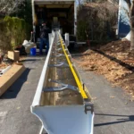 New white seamless rain gutter being prepared for installation on a driveway.