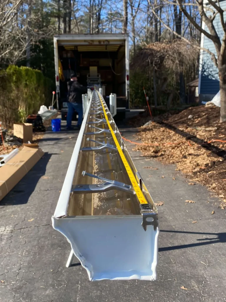 New white seamless rain gutter being prepared for installation on a driveway.